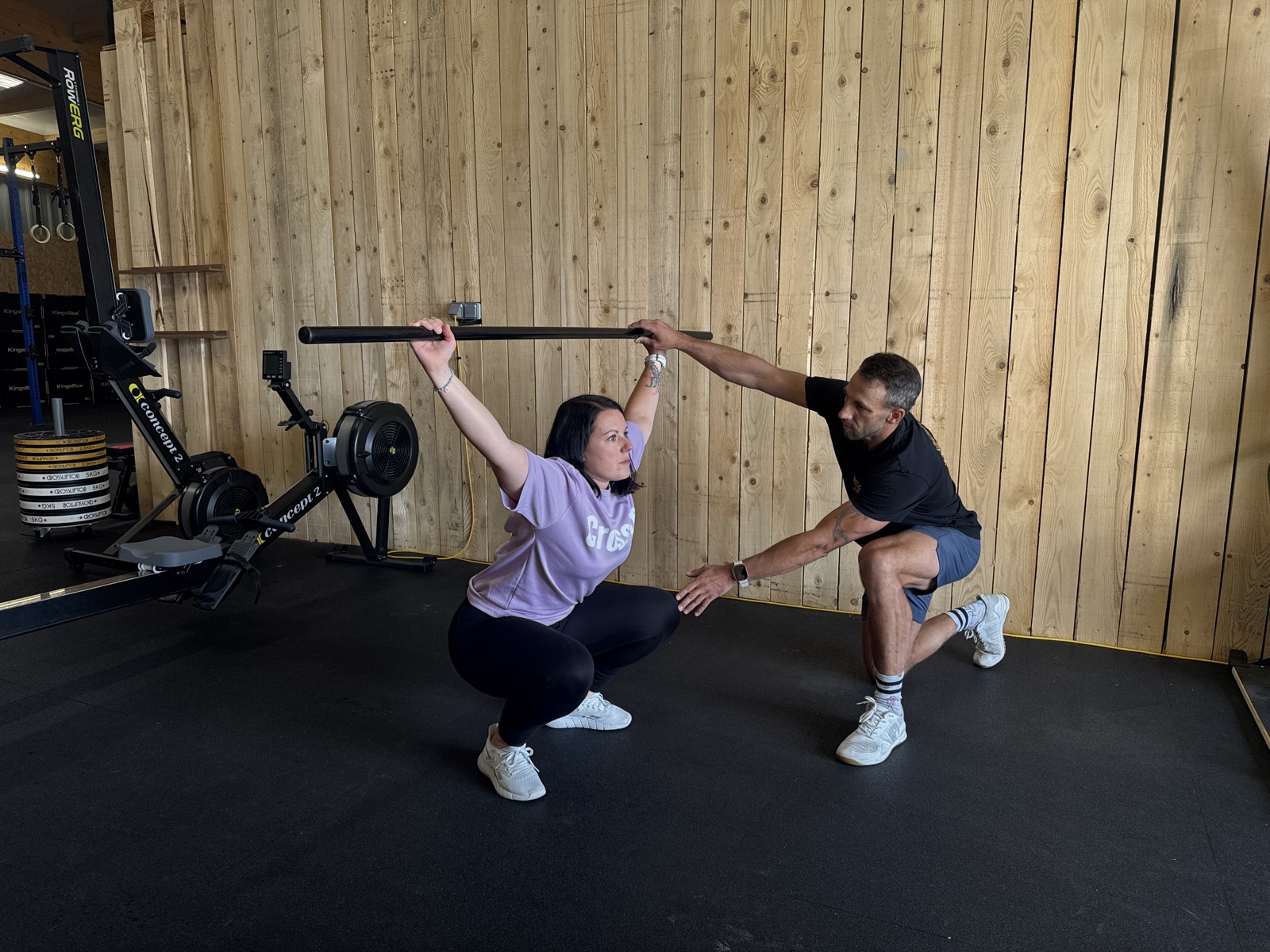 Un coach corrige la position de squat d une adherente debutante, barre a vide