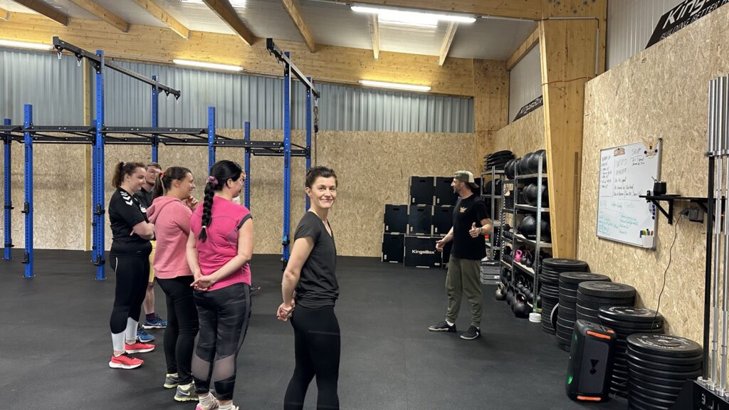 Un coach briefe un groupe d'adhérents avant la séance, devant le rig et le tableau du WOD, à CrossFit Hormesis